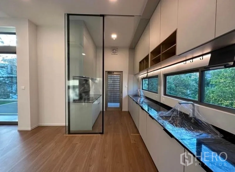 Detached House for rent - Long galley kitchen with black countertops, tall glass partition and side windows.