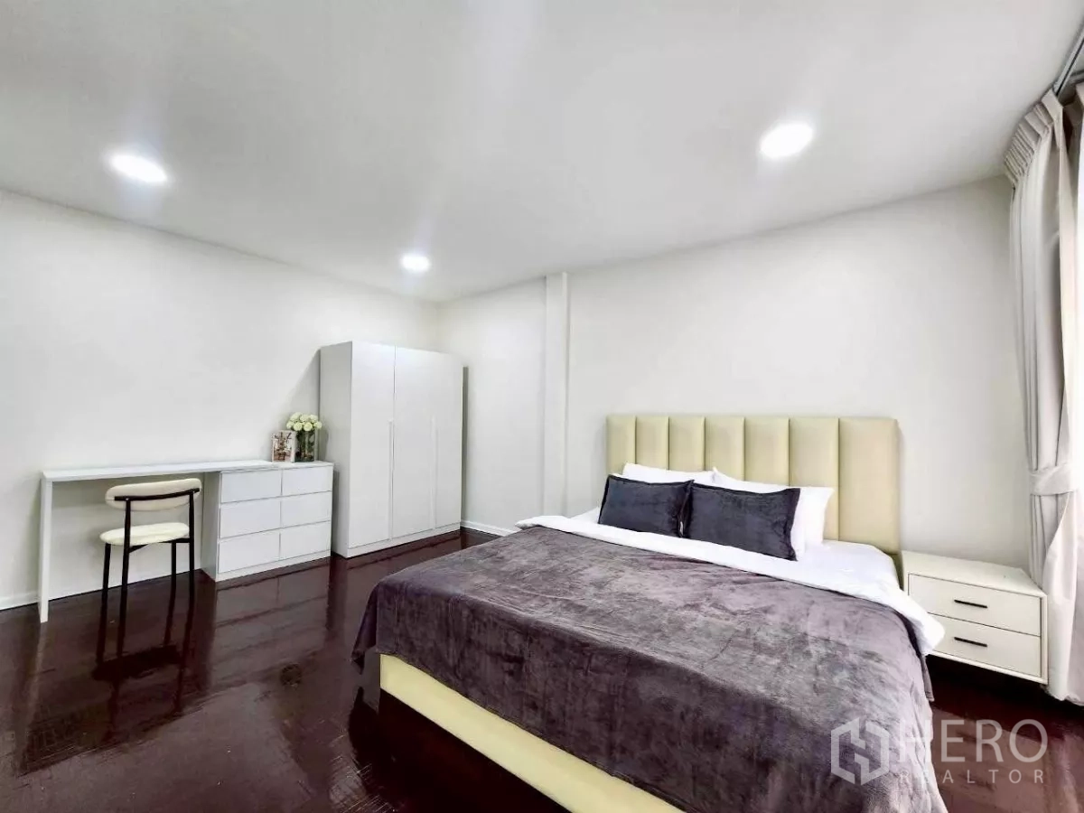 Townhouse for rent in Huai Khwang, Bangkok - Large guest bedroom with king bed, dark wood floors, wardrobe and work desk.