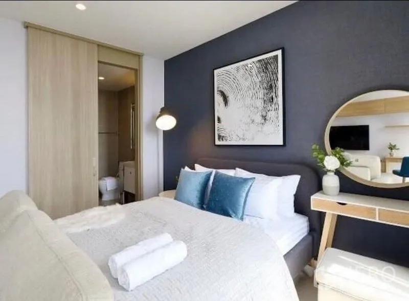 Condominium for rent in Pathum Wan, Bangkok - Bedroom suite with blue accents, round vanity mirror, and doorway to the bathroom.
