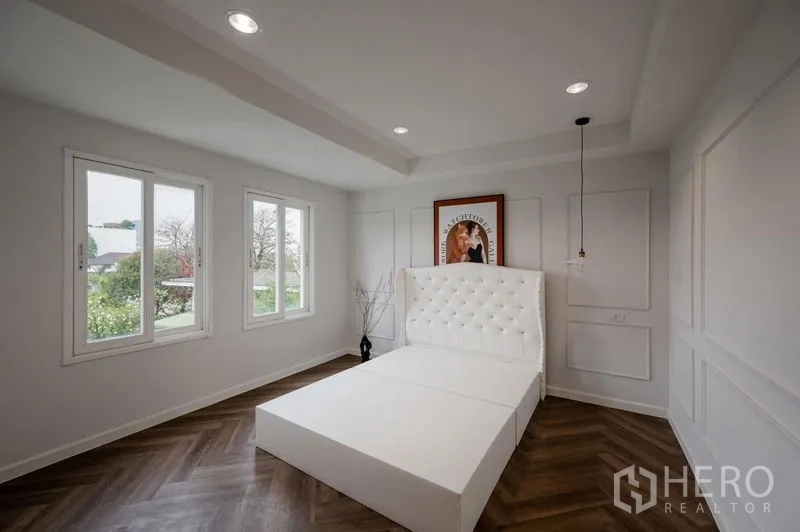 Townhouse for sale - Corner bedroom with three windows, tufted white headboard and herringbone flooring.
