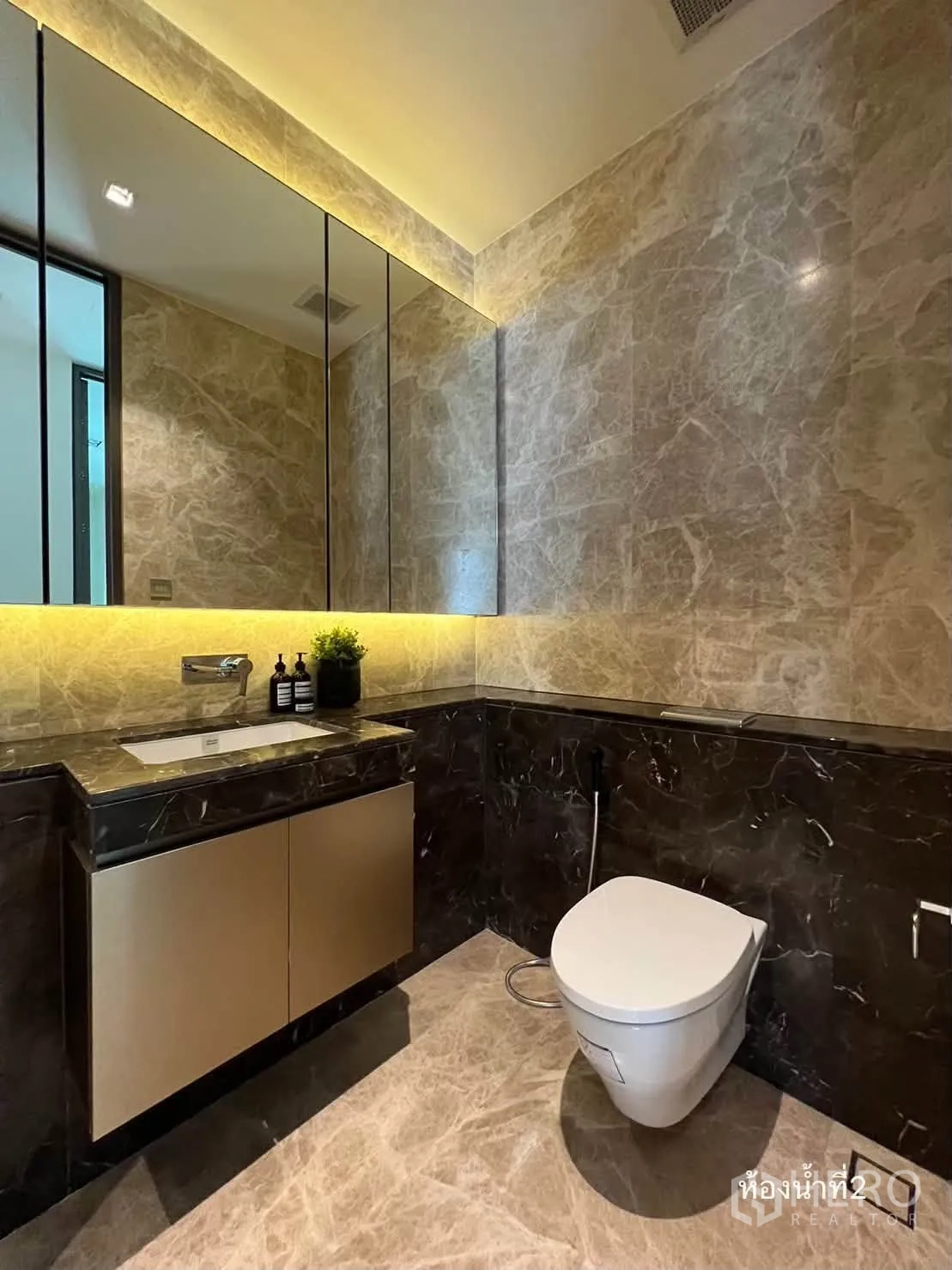 Condominium for rent in Pathum Wan, Bangkok - Marble-clad bathroom with backlit mirror, floating vanity, and toilet.