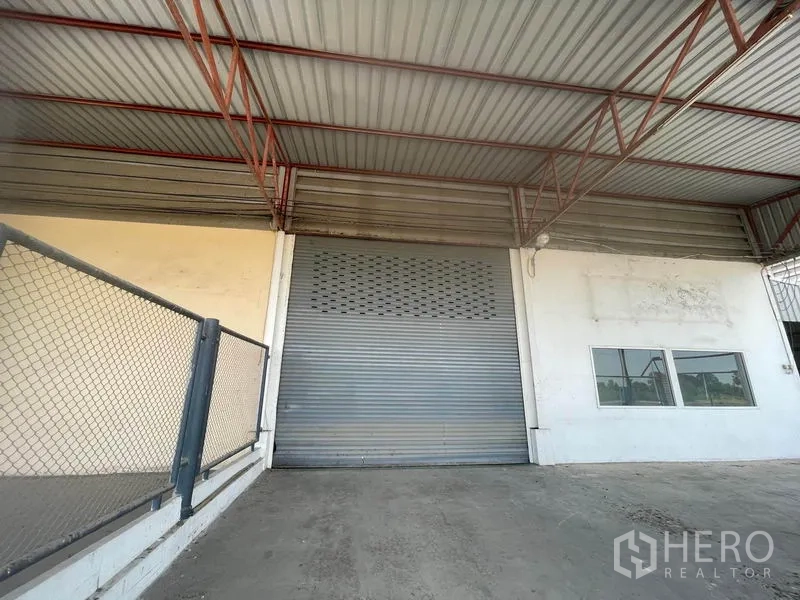 Factory for rent in Lat Lum Kaeo, Pathum Thani - Close-up of warehouse roller shutter beneath steel-truss roof next to office windows.