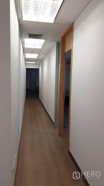 办公空间 出租在Bang Rak, Bangkok - 明亮走廊，木地板与白色墙面，天花荧光灯，通往独立房间。