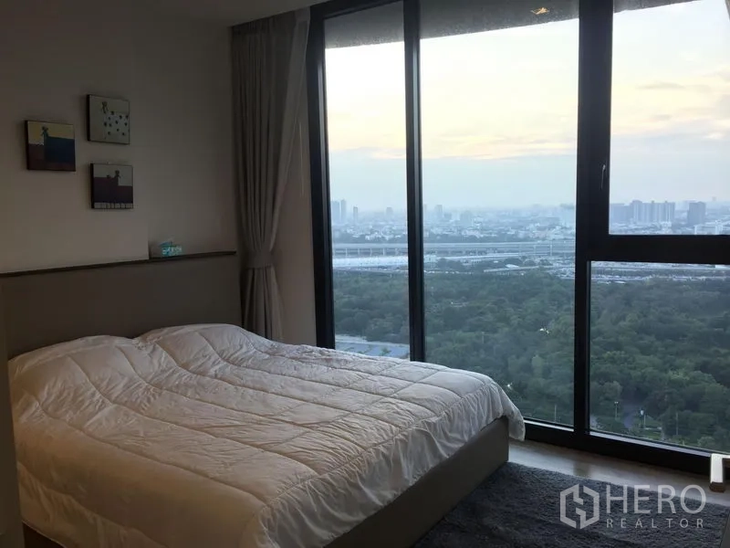 公寓 出租在Chatuchak, Bangkok - 卧室配落地窗，可欣赏公园与城市天际线景观。