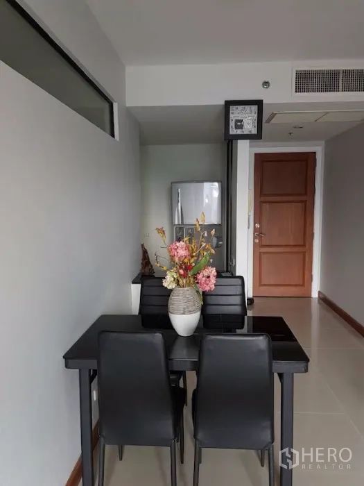 Condominium for rent in Watthana, Bangkok - Dining nook with black four-seat table and flower centerpiece, view to entrance door and refrigerator.