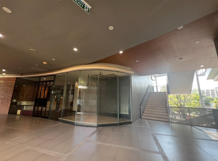 Retail Space for rent in Khlong Toei, Bangkok - Empty retail unit with curved floor-to-ceiling glass frontage beside a stairway in a modern Sukhumvit mall.