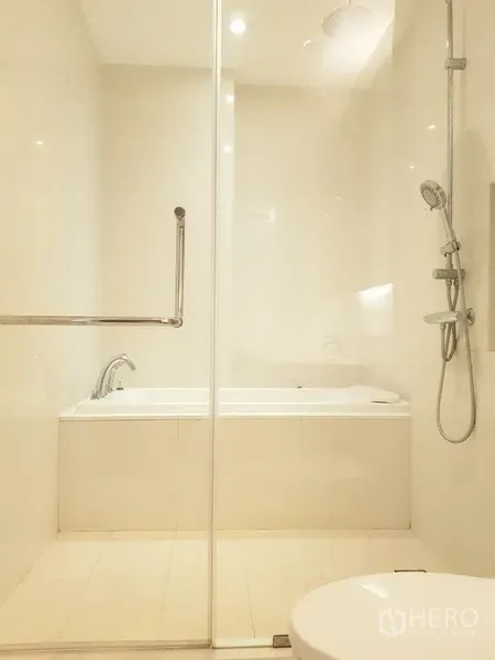 Condominium for rent in Khlong Toei, Bangkok - Bright bathroom with a glass-enclosed shower and separate bathtub in neutral tones.