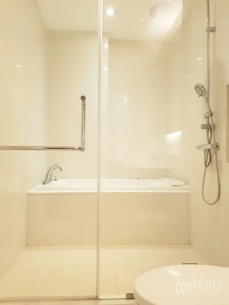 Condominium for rent in Khlong Toei, Bangkok - Bright bathroom with a glass-enclosed shower and separate bathtub in neutral tones.