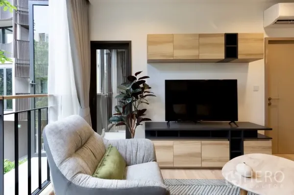 Condominium for rent or sale in Watthana, Bangkok - TV wall with wood cabinets, indoor plant and sliding door to the balcony.