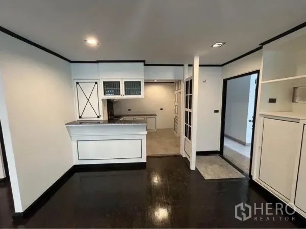 Condominium for rent or sale in Watthana, Bangkok - Open-plan living and kitchen with breakfast bar and glossy dark flooring.