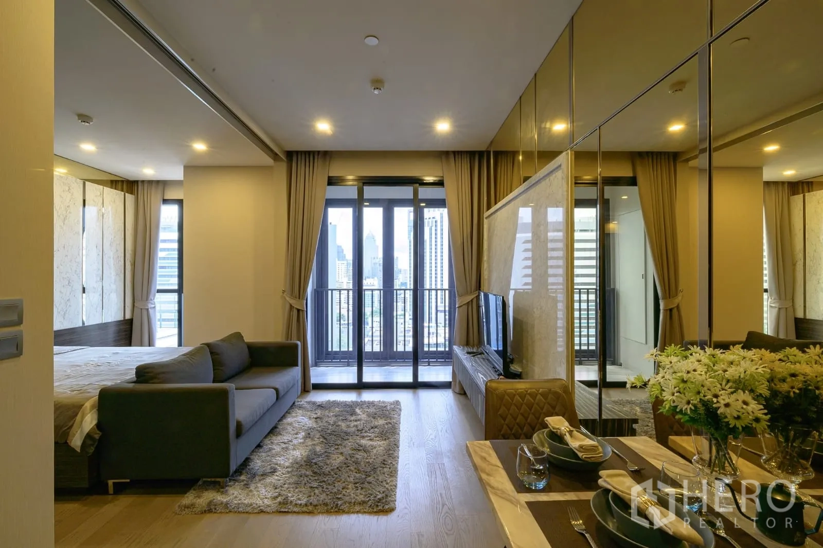 Condominium for rent in Watthana, Bangkok - Open-plan living and bedroom with balcony doors, city view and a mirrored dining nook.