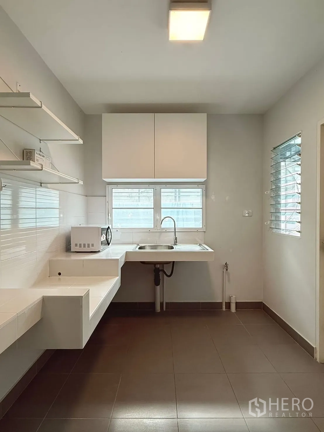Detached House for rent in Bang Phli, Samut Prakan - Minimal kitchen with white countertops, sink, wall shelves, and windows.