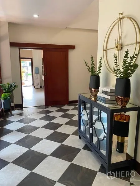 Detached House for rent in Suan Luang, Bangkok - Hallway with sliding wooden door, checkered tiles, decorative clock and console.