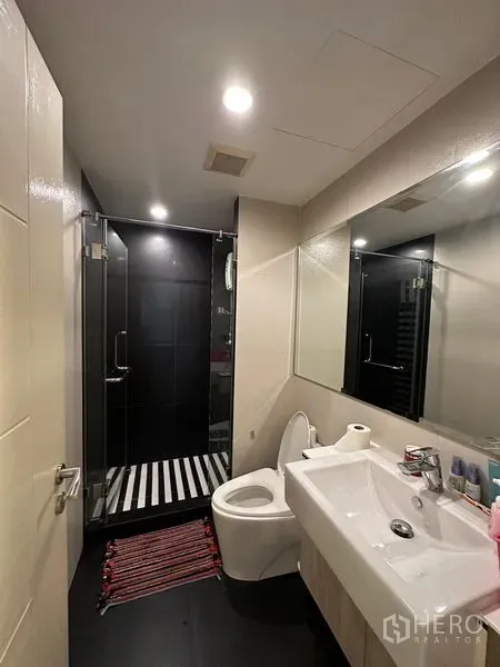 Condominium for rent in Khlong Toei, Bangkok - Contemporary bathroom with glass shower, black tile wall, vanity and toilet.