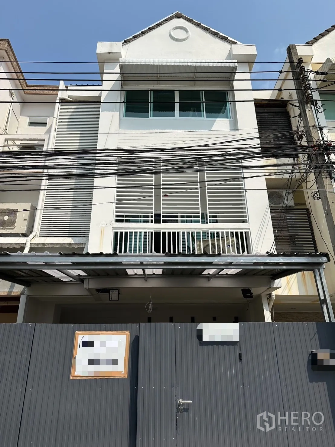 联排别墅 for rent in Watthana, Bangkok - 三层白色联排别墅外立面，带金属大门与阳台百叶。