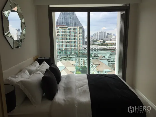 Condominium for sale in Bang Rak, Bangkok - Bedroom with large window showcasing Bangkok skyline and a geometric wall mirror.