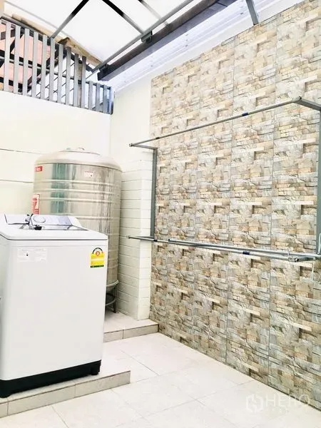 联排别墅 出租在Prawet, Bangkok - 带顶洗衣区，配洗衣机、不锈钢水塔与石纹墙面。
