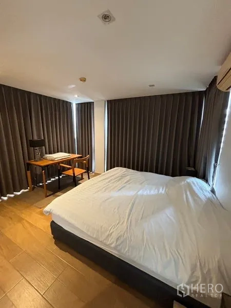 公寓 出租在Watthana, Bangkok - 主卧配大床，转角落地窗旁设书桌与遮光帘。