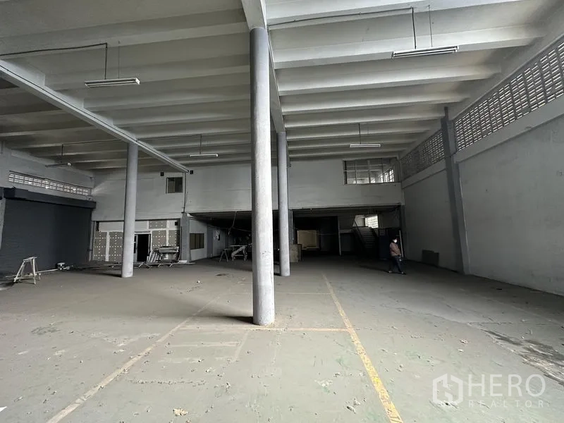 Home Office for rent in Khan Na Yao, Bangkok - Open industrial floor space with central columns, fluorescent lighting, shutter access and mezzanine rooms.