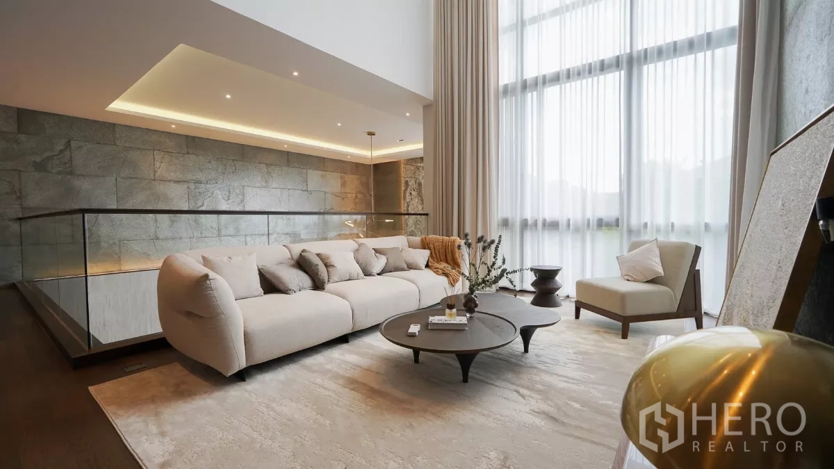 Detached House for rent or sale in Bang Kapi, Bangkok - Second-floor family room with plush sofa and coffee tables beside sheer curtains.