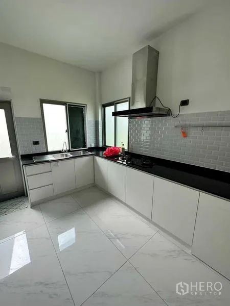 Detached House for rent in Lat Krabang, Bangkok - Modern kitchen with white cabinetry, black stone countertops, range hood and tiled floor.