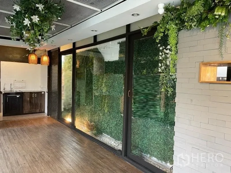 Retail Space for rent in Watthana, Bangkok - Retail area with floor‑to‑ceiling windows, faux green wall, wood floors and a service counter with pendant lights.