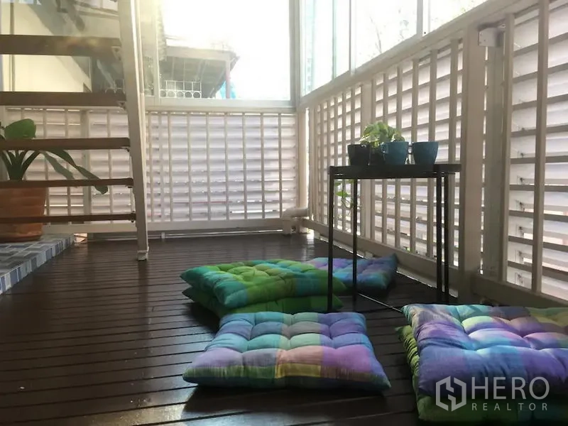 联排别墅 出租在Bang Rak, Bangkok - 封闭式阳台，木地板、格栅墙，地垫、摆放盆栽的小桌与楼梯。