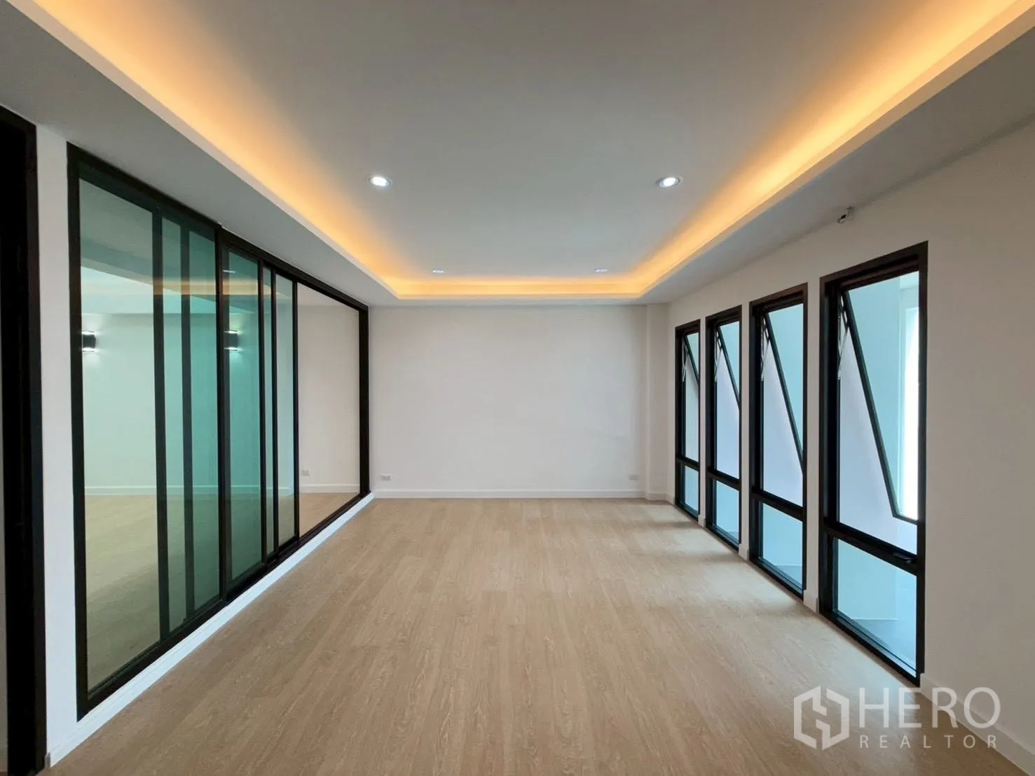Townhouse for sale in Phra Khanong, Bangkok - Long room with cove lighting, multiple awning windows, and a glass partition.