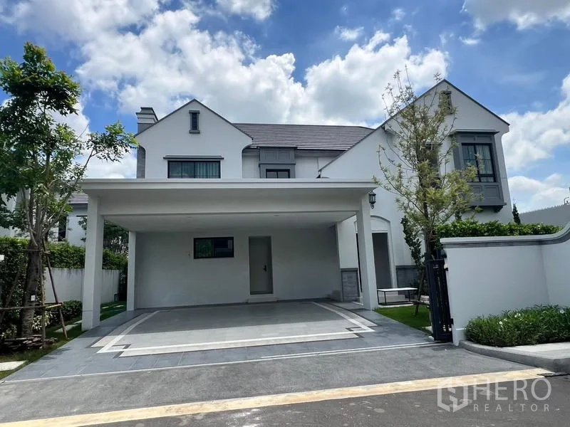 Detached House for rent or sale in Saphan Sung, Bangkok - Modern white two-storey detached house with covered two-car carport and gate under a blue sky.