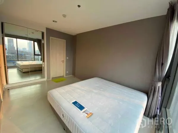 Condominium for rent or sale in Khlong Toei, Bangkok - Bright bedroom with mirrored wardrobe and floor‑to‑ceiling windows facing the skyline.