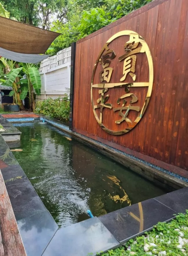 独立式住宅 出租在Bang Kapi, Bangkok - 花园锦鲤池与木质景墙，饰有金色标志。