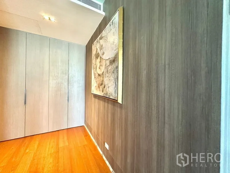 Condominium for rent in Pathum Wan, Bangkok - Corridor with tall wardrobes, wood flooring and framed artwork.