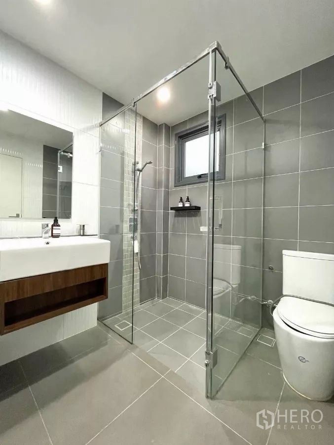 Detached House for rent in Saphan Sung, Bangkok - Modern bathroom with glass shower enclosure and gray tiles.