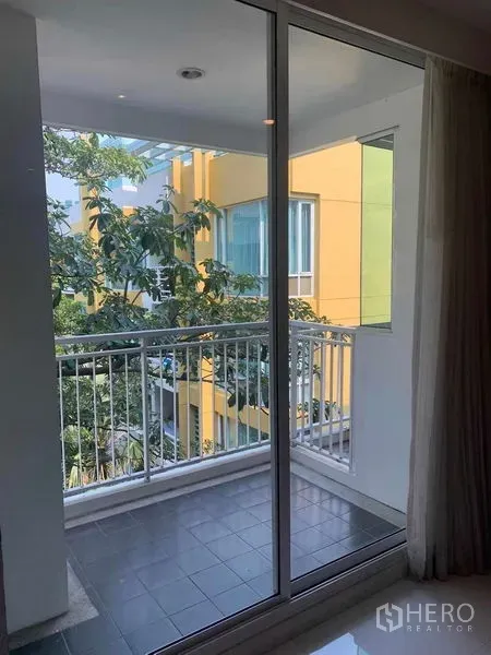 Condominium for rent or sale in Khlong Toei, Bangkok - Balcony with sliding glass door overlooking trees and a neighboring building.