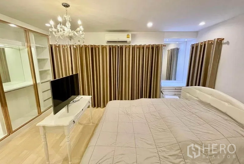 Townhouse for sale in Wang Thonglang, Bangkok - Master bedroom featuring chandelier, air conditioning, built-in wardrobe and TV stand over warm wood floors.