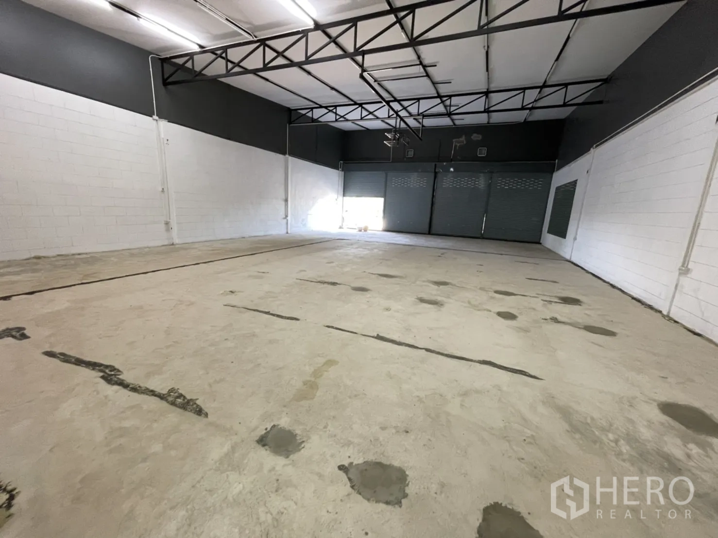 Warehouse for rent in Lam Luk Ka, Pathum Thani - Wide warehouse bay with smooth concrete floor, painted block walls and shuttered frontage.