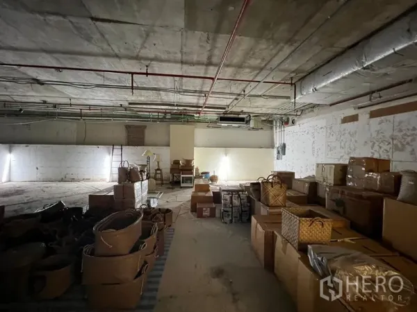 Retail Space for rent - Open interior with low lighting, concrete floor and stacked boxes in a large retail space under renovation.
