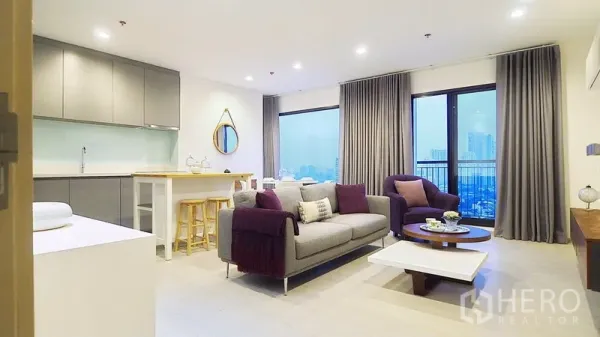 Condominium for rent or sale in Khlong Toei, Bangkok - Open-plan living room with sofa and armchair, balcony city view, and kitchen with island breakfast bar.