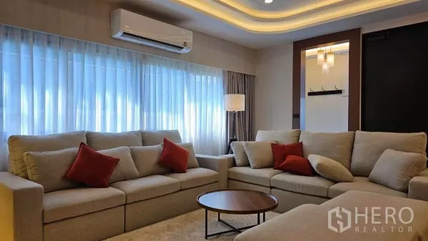Detached House for rent in Bang Phli, Samut Prakan - Bright living room with beige sofas, red cushions and cove ceiling lighting.