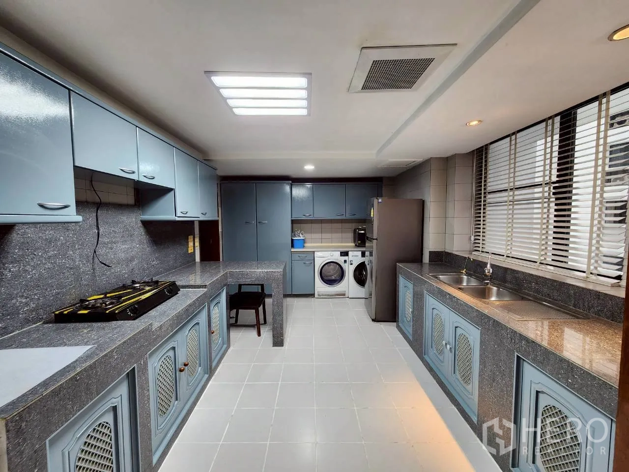 Condominium for rent in Khlong Toei, Bangkok - Full-size kitchen with granite counters, blue cabinets, gas hob, double sink and laundry machines.