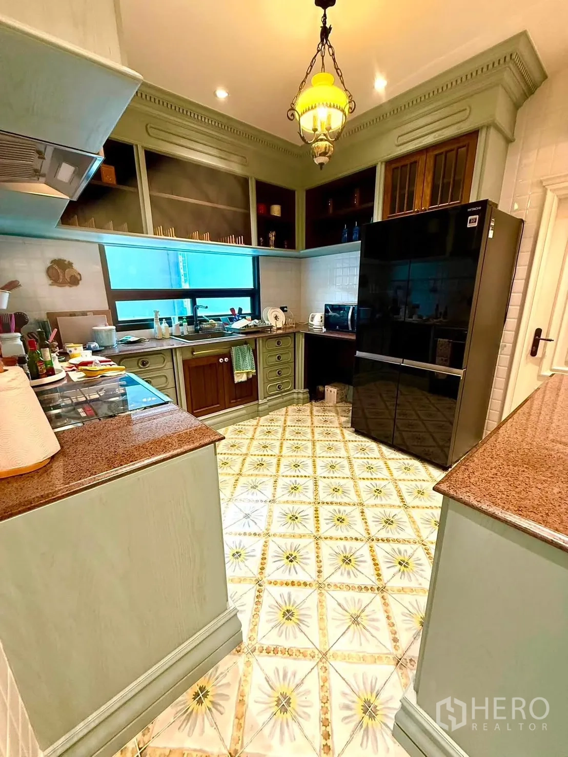 Detached House for rent in Bang Kapi, Bangkok - U-shaped kitchen with window, cooktop, and decorative floor tiles.