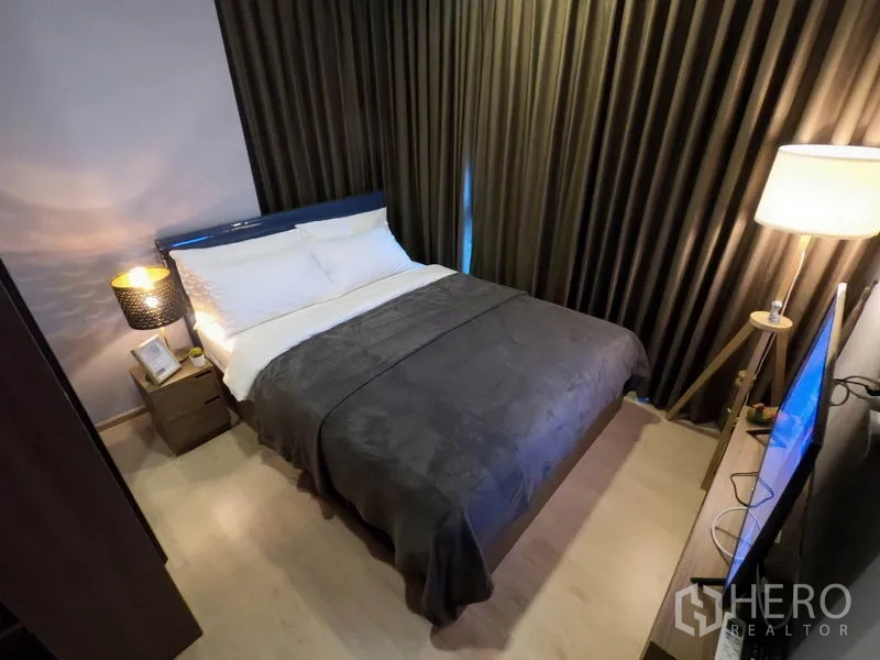 公寓 出租或出售在Watthana, Bangkok - 温馨次卧，双人床、遮光窗帘、落地灯与电视。