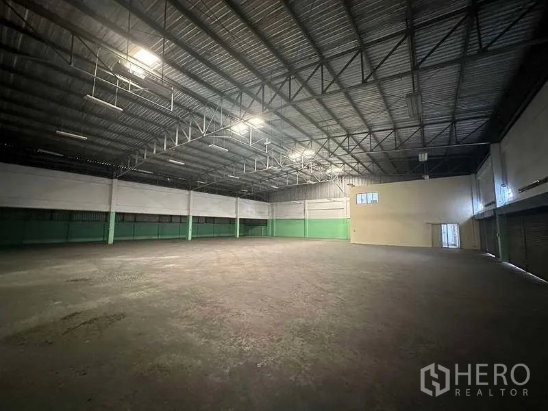 Factory for rent in Nonthaburi - Open production space with trussed ceiling, green lower walls and loading shutters along one side.
