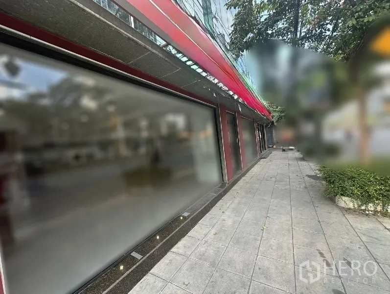 Retail Space for rent in Bang Rak, Bangkok - Extended glass shopfront beneath a red awning along the sidewalk with trees nearby.