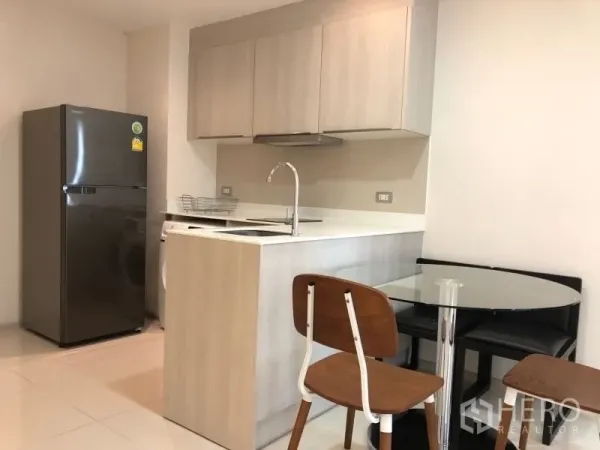 Condominium for sale in Khlong Toei, Bangkok - Modern light‑wood kitchen with island sink, large fridge and a round glass dining table.