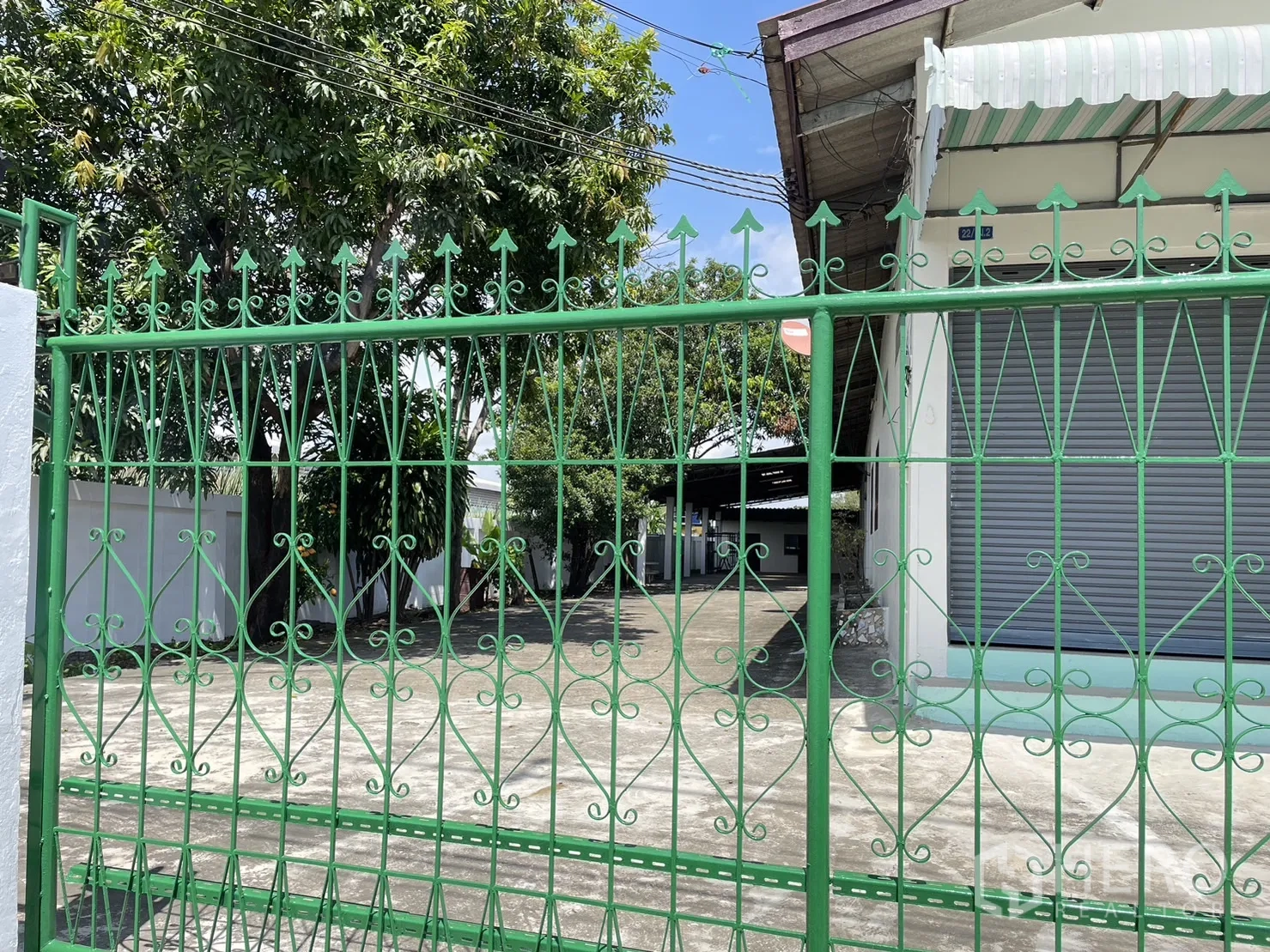 工厂 出租或出售在Pathum Thani - 绿色铁艺入口门，内侧可见车道与树木。