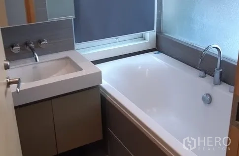 Condominium for rent in Khlong Toei, Bangkok - Bathroom with soaking bathtub, vanity sink and frosted window for natural light.
