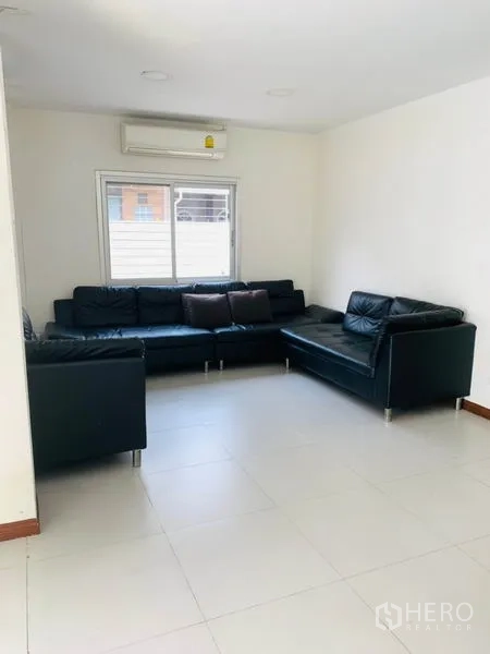 Townhouse for rent or sale in Huai Khwang, Bangkok - Corner lounge with L-shaped black leather sofa, air conditioner and window blinds