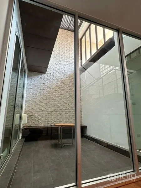 Townhouse for sale in Yan Nawa, Bangkok - Indoor courtyard atrium with tall brick feature wall and wide sliding glass doors.