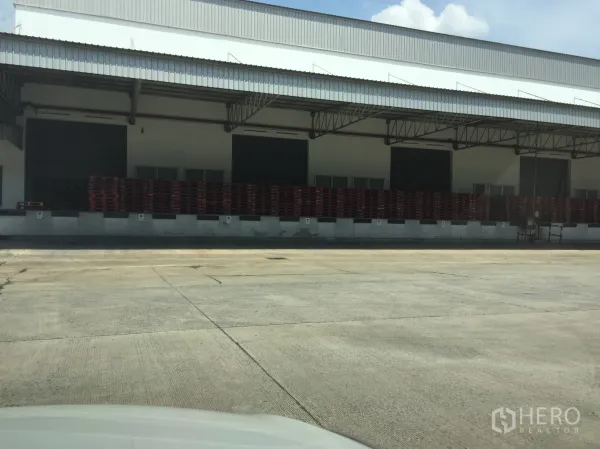 货栈 出租在Khlong Luang, Pathum Thani - 近景：多扇卷帘装卸门、整齐堆放的托盘以及宽阔的混凝土车场。